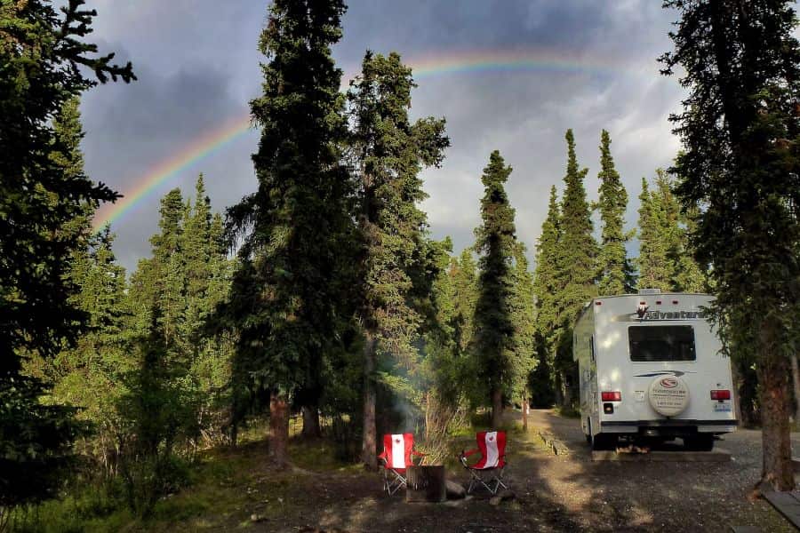 Camper van Fraserway in het bos van Canada met een regenboog op de achtergrond.
