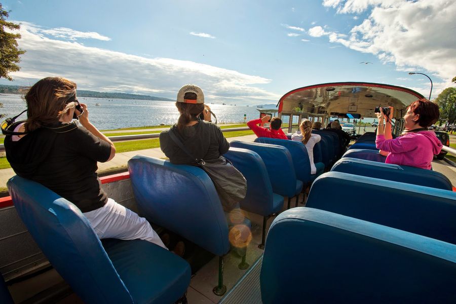 Mensen op het open dak van een bus tijdens een Hop-On Hop-Off tour in Vancouver in Canada.