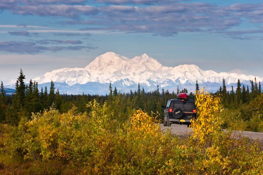 Een auto op de weg in Alaska met de bergen van Denali National Park op de achtergrond.