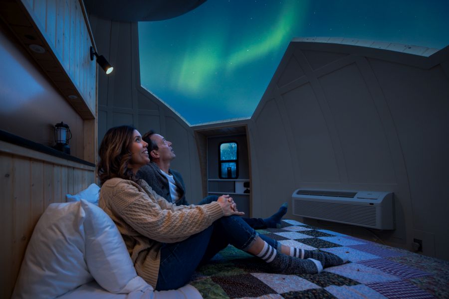 From inside the dome a couple is looking up at the  aurora borealis in the night sky.