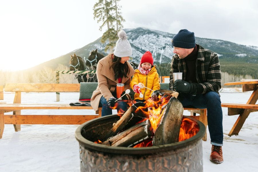 Familie roosteren marshmallows bij het vuur in Banff tijdens een winterreis naar Canada