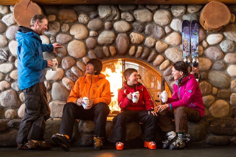 Gezin drinkt warme chocomelk bij de open haard bij Lake Louise ski resort tijdens een winterreis naar Canada