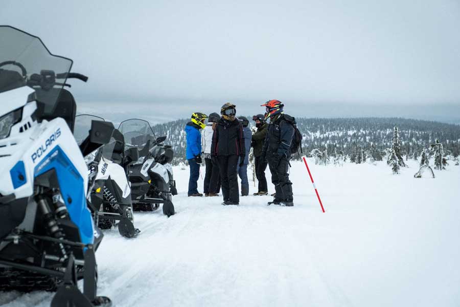 Groepje mensen op de berg naast hun sneeuwscooter